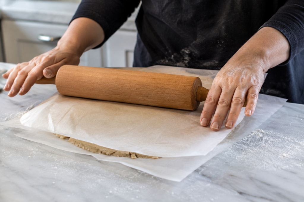 Gluten free pie dough being rolled out between parchment paper sheets on a lightly floured surface.